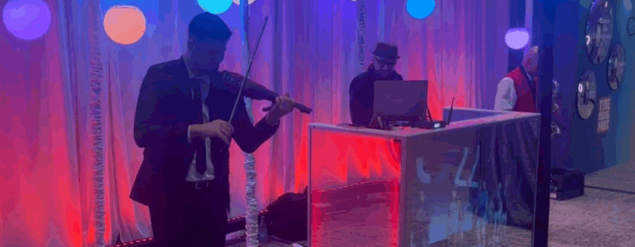 A man playing a violin in front of a stage with a man in a suit.